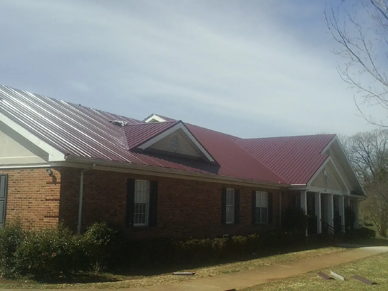 Red metal roof with gabled entries on a long brick building, from a Hail Damage Roof Repair job in Saxonburg
