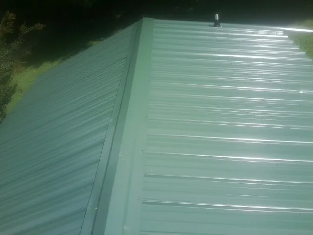 New green metal panels meeting at the ridge of a roof — Flat Roof Repair work by our crew in Saxonburg