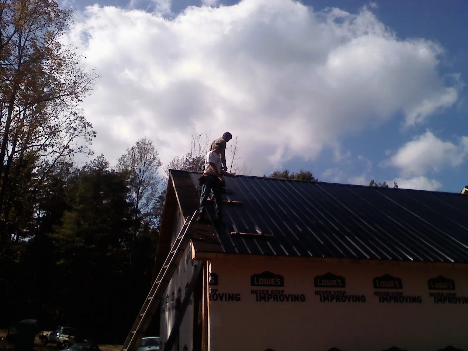 Roofer fastening dark metal panels high against a cloudy sky, from a Roof Inspection job in Saxonburg