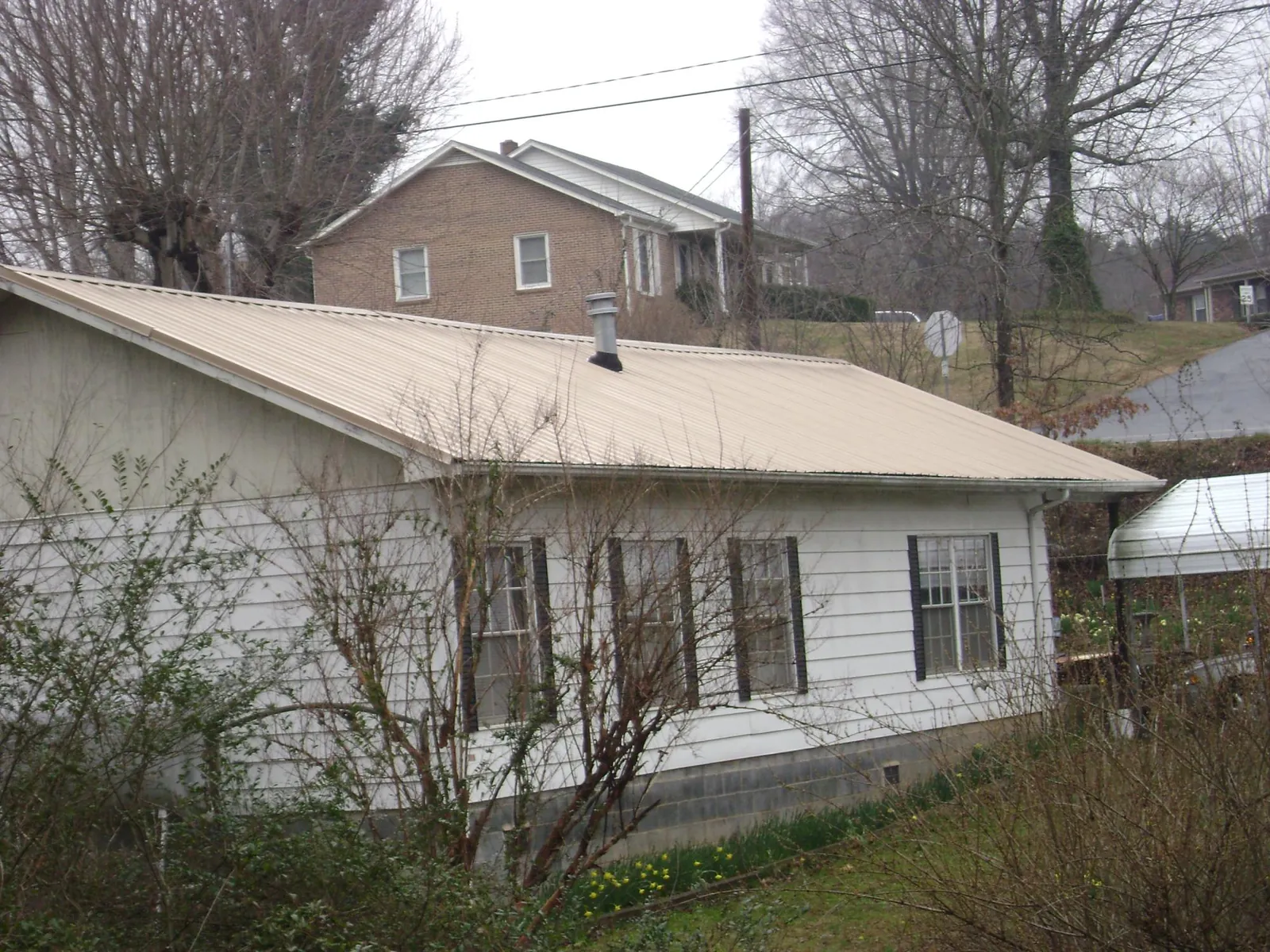 Tan metal roof on a white sided house set into a hillside — Commercial Roofing by Roofing Brothers in Saxonburg